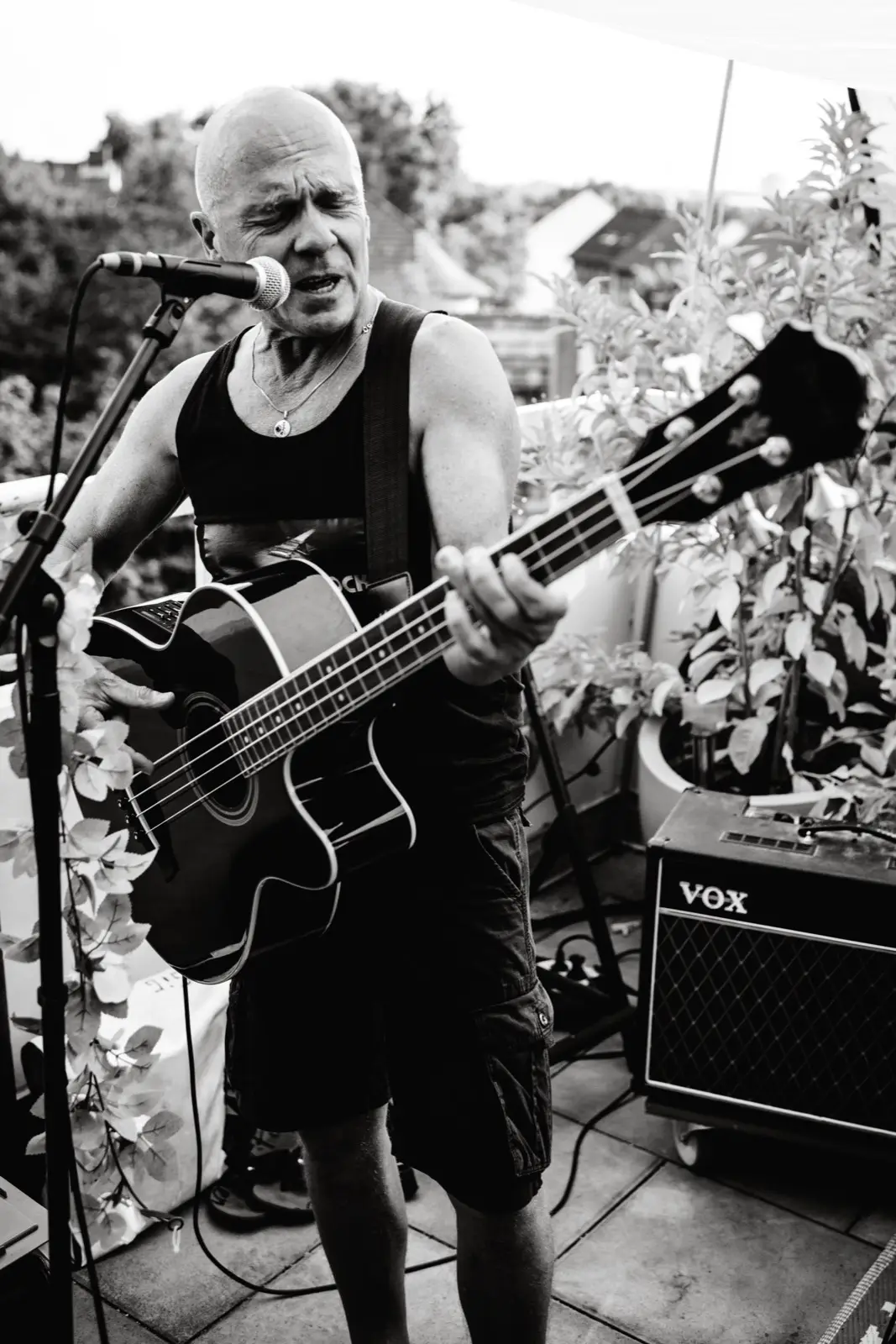 Andreas spielt einen Akustikbass und singt ins Mikrofon, rechts neben ihm ein Vox-Verstärker.