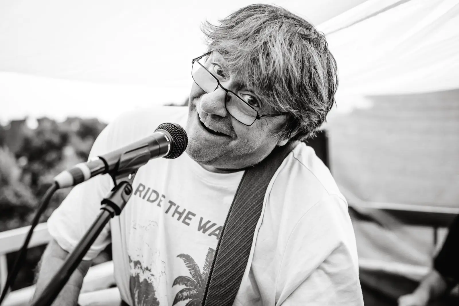 Bernhard Röhrenbeck lächelt hinter dem Mikrofon, den Gitarrengurt über der Schulter.