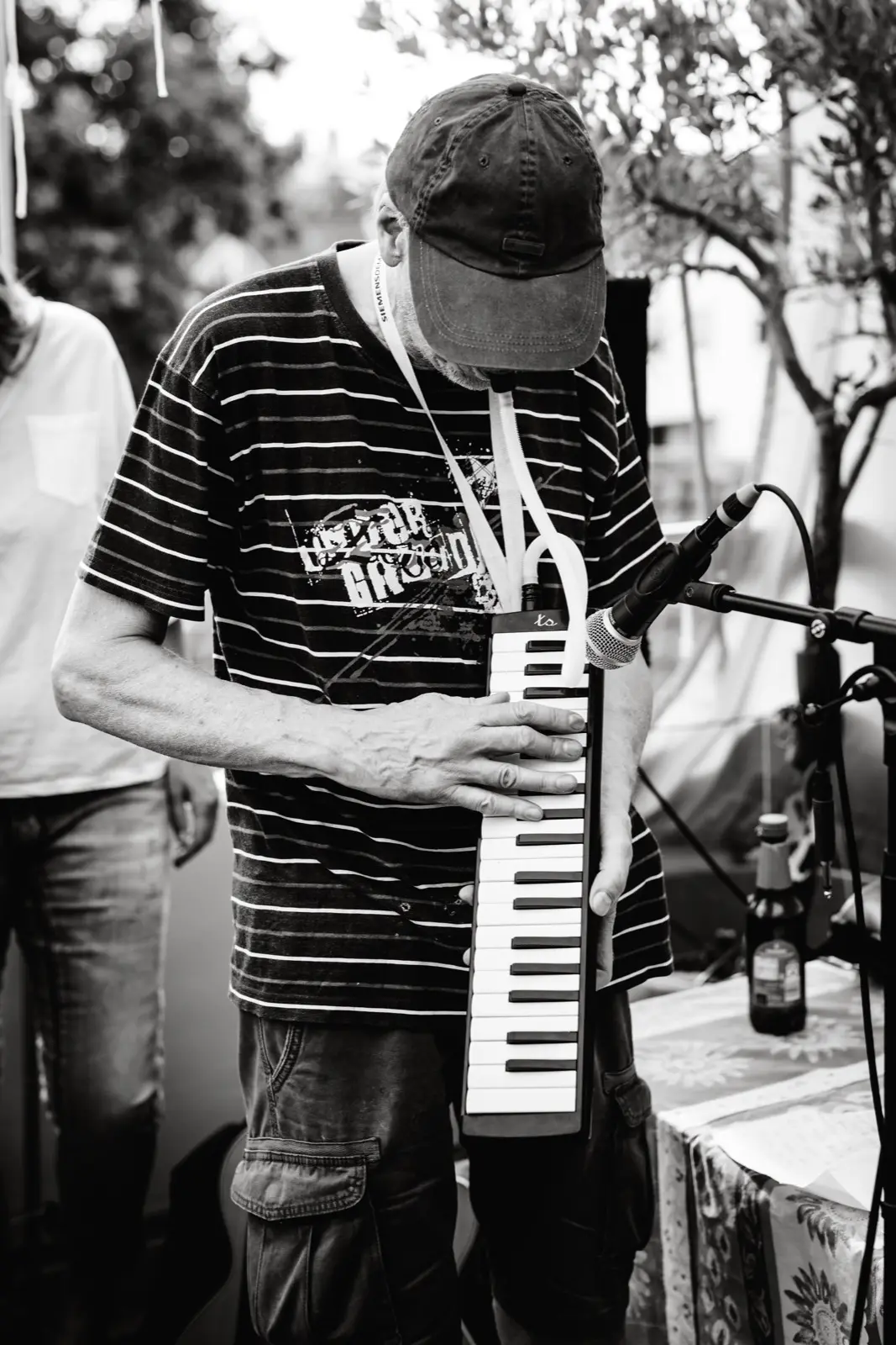Kurt Ludwig mit Cap spielt eine umgehängte Melodica vor dem Mikrofon.