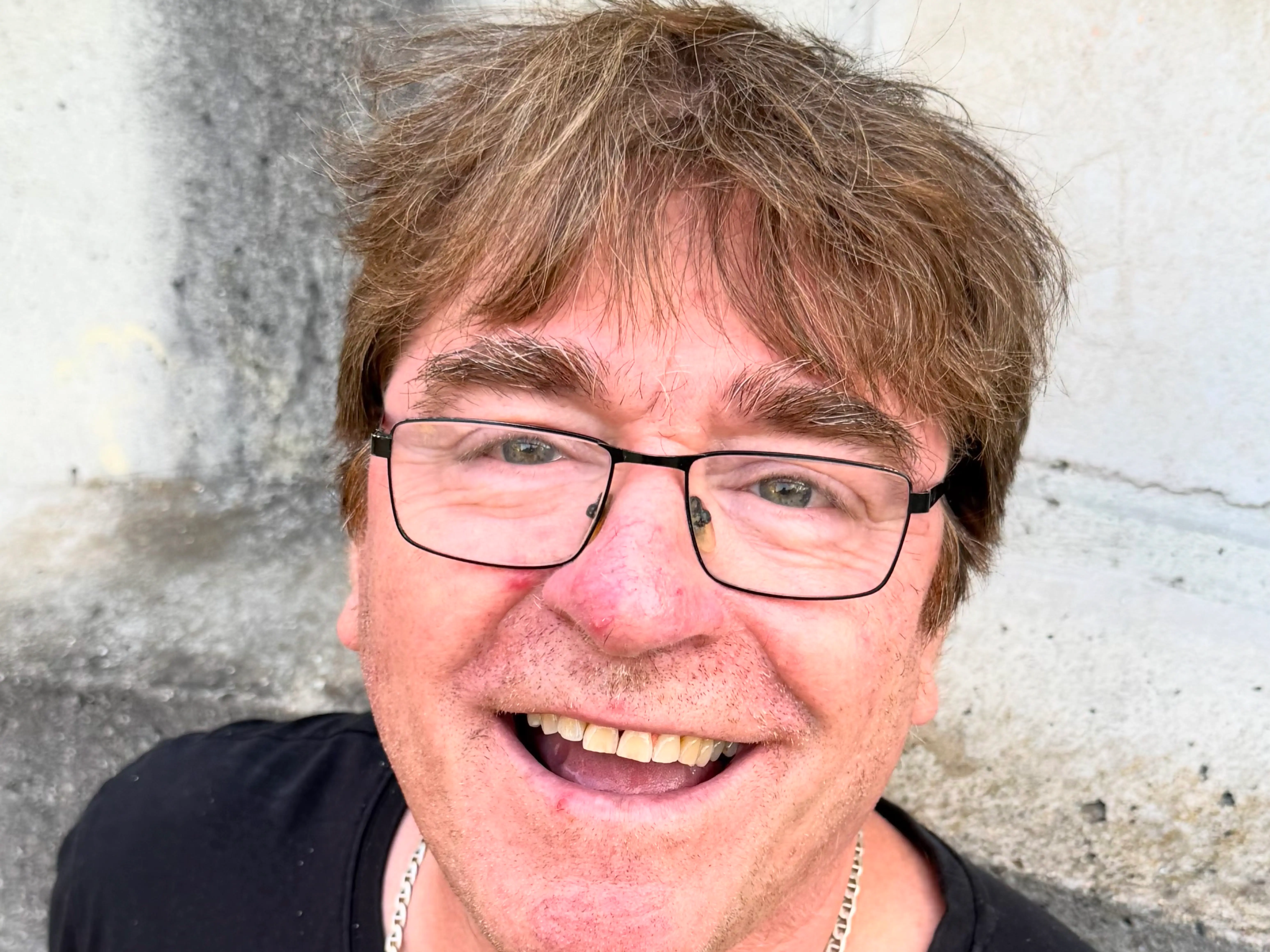 Bernhard Röhrenbeck, lachend, mit Brille und einem T-Shirt mit bunten Gitarren