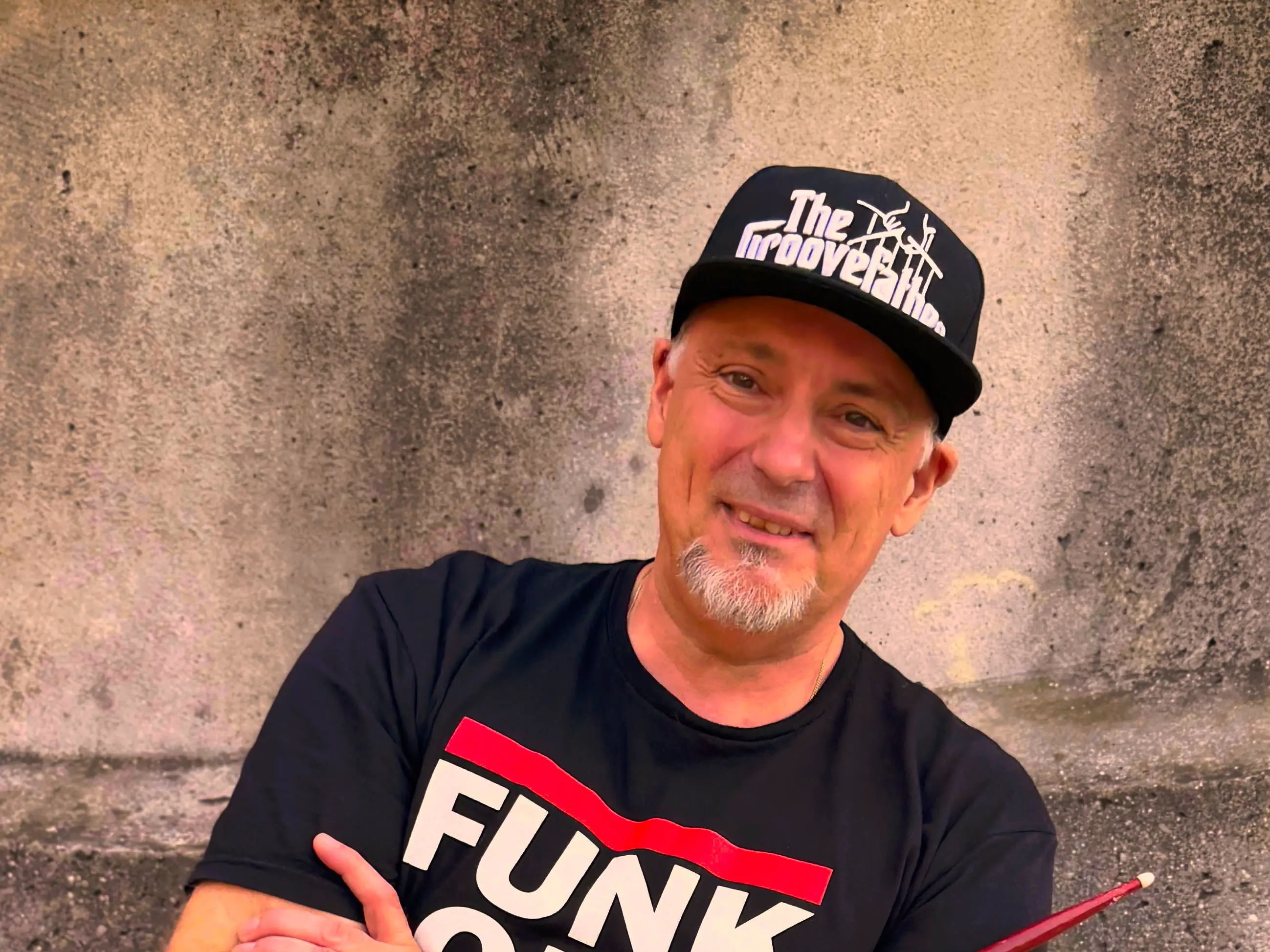 Thomas Südbröcker mit Cap und Drumsticks, vor einer Betonwand